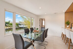 Uma área de refeições moderna com uma mesa de vidro, cadeiras pretas e vista para um corpo de água.