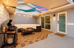 An outdoor patio with a grill, seating area, and a covered space with string lights. - Cape Coral Luxury 5BR Pool, Spa, Dock, Game Room (Cape Coral)