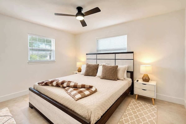 A bedroom with a bed, a ceiling fan, bedside lamps, and a window.