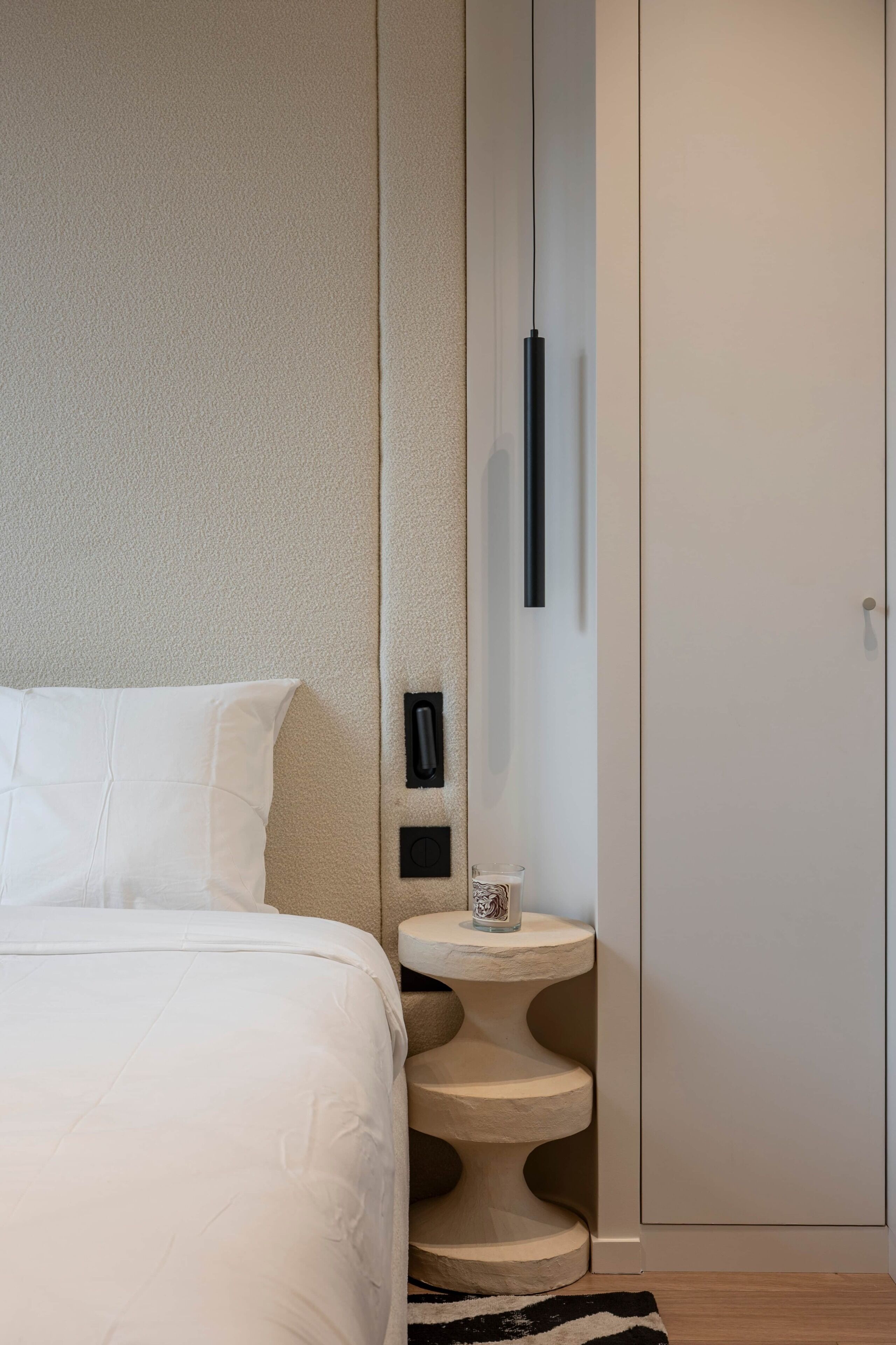 A bedroom with a bed, a bedside table with a cup, a mirror, and a wardrobe.