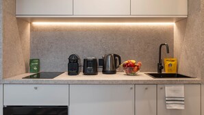 Et moderne køkken med indbygget komfur, kaffemaskine, elkedel og en skål med frugt på bordpladen.