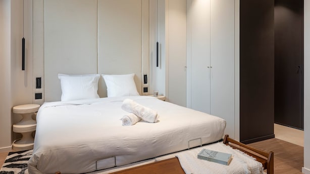 Et moderne hotelværelse med en stor seng, et sengebord, en indbygget garderobe og en mørk dør.