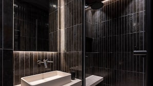A modern bathroom with a rectangular sink, a handheld showerhead, and a glass-enclosed shower area.