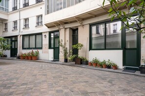 A street with a row of terracotta potted plants and a building with green doors and windows. - Deluxe Suite between Concorde and Vendôme (Paris)