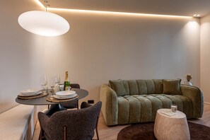 Un salon moderne avec un coin repas, comprenant une table ronde dressée pour deux personnes, un canapé et une table basse ronde originale.