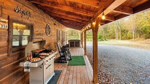 En utomhusplats med tak, utrustad med en grill, sittplatser och utsikt över den omgivande skogen.