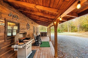 An outdoor covered patio with a barbecue grill, seating, and a view of the surrounding forest. - Mountaintop Log Cabin with Hot Tub, Pool & Fire Pit (Sevierville)