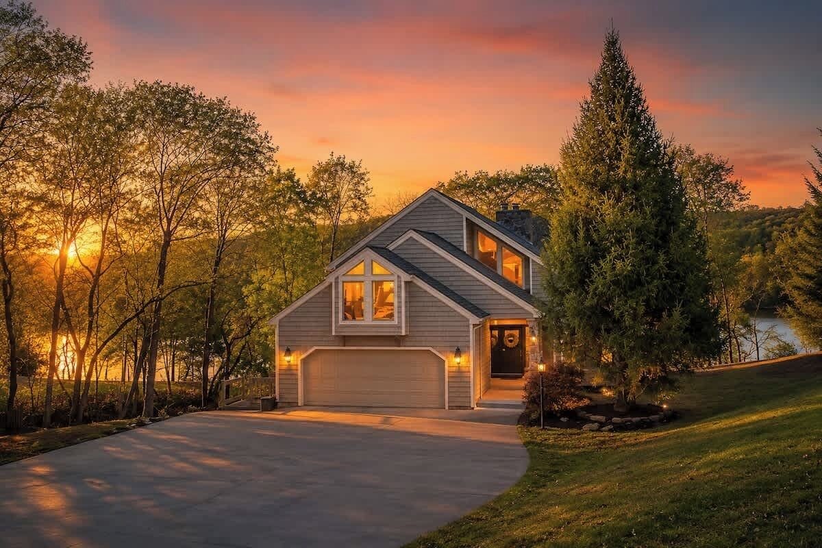 Une maison de plain-pied avec un garage, entourée d’arbres et dotée d’une allée.