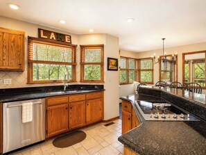 A kitchen with wooden cabinets, a stainless steel dishwasher, a granite countertop, and a large island with a built-in stove.