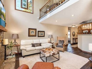 A spacious living room with a high ceiling, a staircase, and a view of a mountain.
