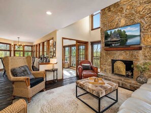 A spacious living room with a stone fireplace, comfortable seating, and a large window overlooking a scenic outdoor area.
