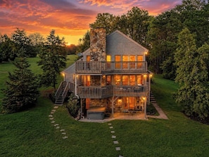 A two-story house with a stone chimney, a balcony, and a covered outdoor seating area.