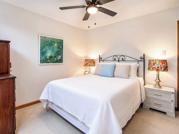 A bedroom with a bed, nightstands, a ceiling fan, and a painting on the wall.
