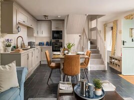 Una cocina moderna con armarios blancos, un comedor con mesa y sillas, y una escalera que sube a un nivel superior.