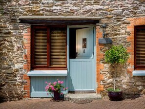 A stone building with a blue door, wooden shutters, and a small potted plant. - Coulscott Stay for Four (Ilfracombe)