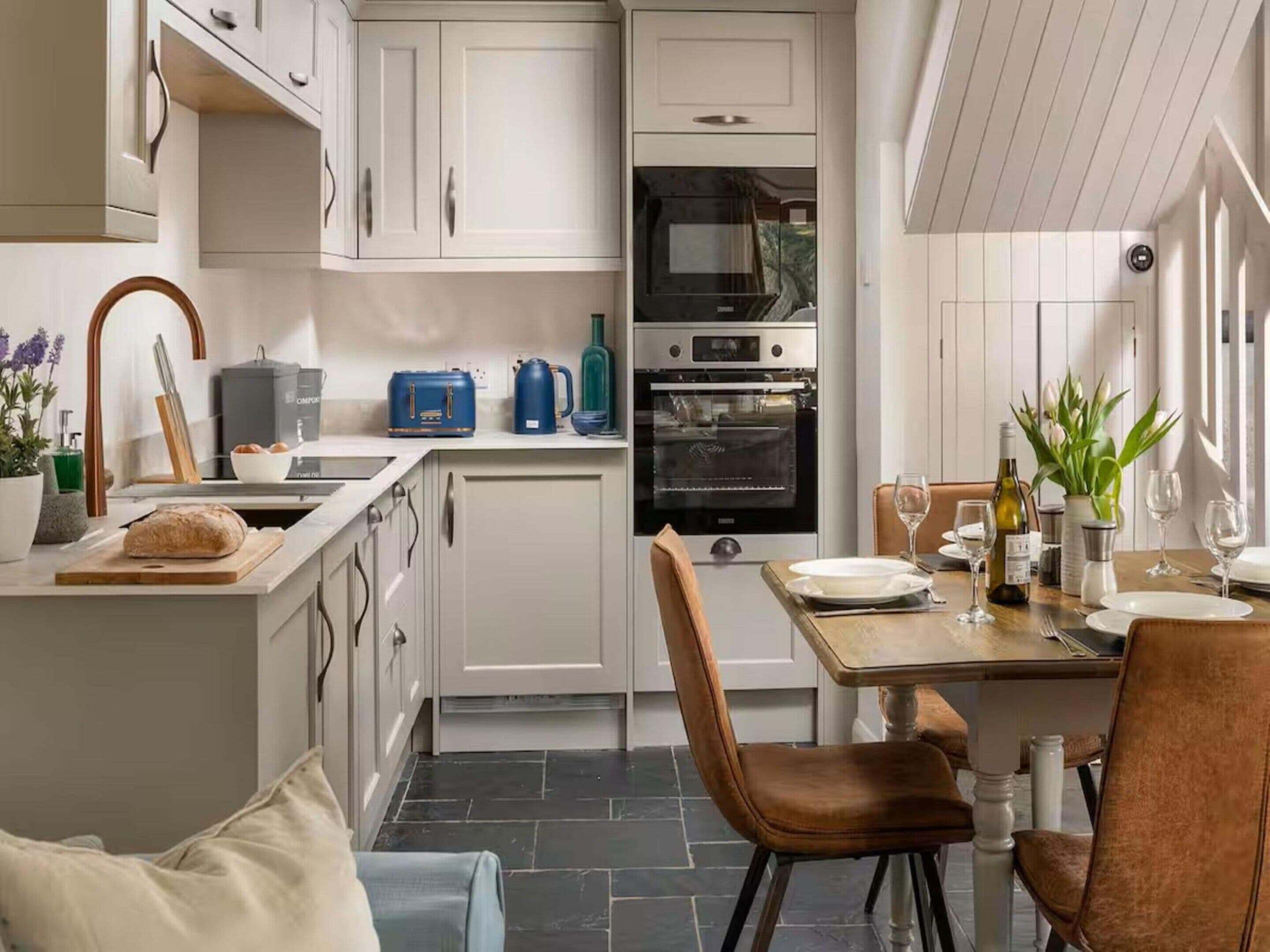 Une cuisine moderne avec des armoires blanches, un four encastré et un coin repas avec une table dressée pour deux personnes.