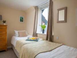 Un dormitorio con dos camas, un aparador, una ventana con cortinas, un cuadro enmarcado y una bandeja con alimentos para el desayuno.