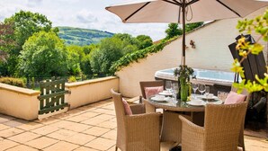 Eine Terrasse im Freien mit Esstisch, umringt von Korbstühlen, einem großen Sonnenschirm und einem Whirlpool.