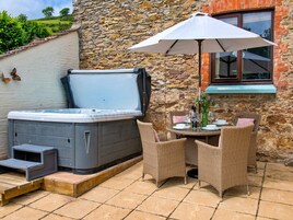 Un jacuzzi con escalones, sillas de mimbre, una mesa con vasos y una botella, y una pared de piedra.