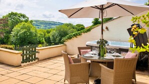 Eine Terrasse im Freien mit Esstisch, umgeben von Korbstühlen und einem großen Sonnenschirm.