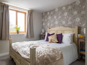 A bedroom with a bed, curtains, a window, a bedside table, and a wall with floral wallpaper. - Coulscott Stay for Four (Ilfracombe)