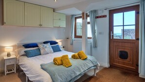 A bedroom with a bed, bedside tables, a wardrobe, a window with curtains, and a view of the outside. - Waterfront Escape With Deck (Torpoint)