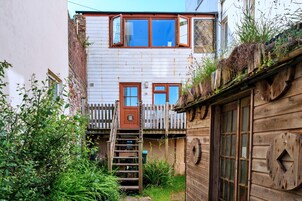 Un estrecho callejón con una escalera de madera que lleva a un edificio blanco con dos ventanas y una puerta visibles.