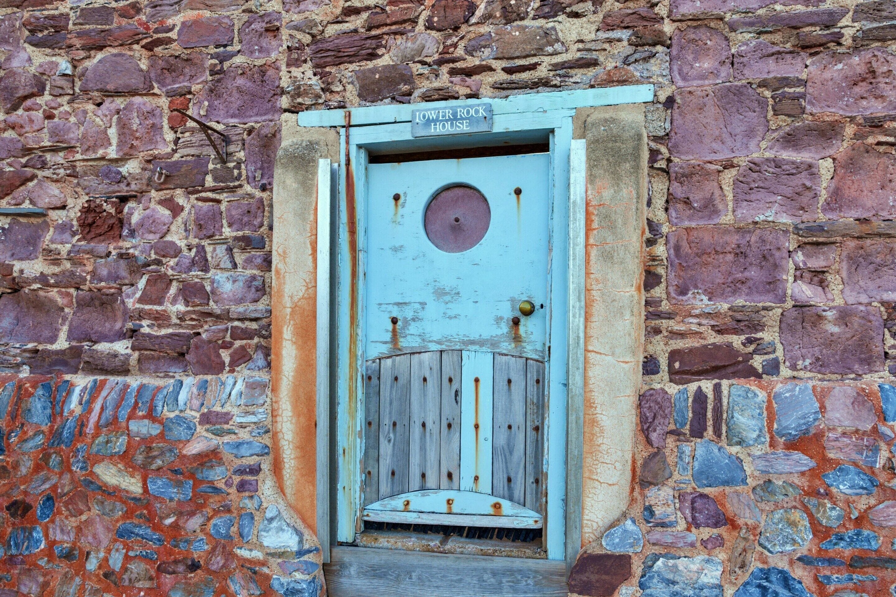 Un mur de pierres rustiques surmonté d’une porte en bois patinée portant l’inscription « LOWER ROCK HOUSE ».