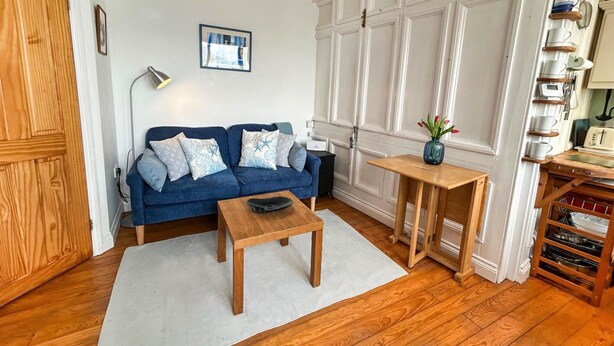 A living room with a blue sofa, a wooden coffee table, a small wooden side table, and a white door with a wooden panel. - Waterfront Escape With Deck (Torpoint)