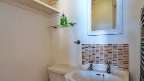 A bathroom with a white sink, a toilet, and a mirror above the sink. There is a green bottle on a shelf above the toilet. - Waterfront Escape With Deck (Torpoint)