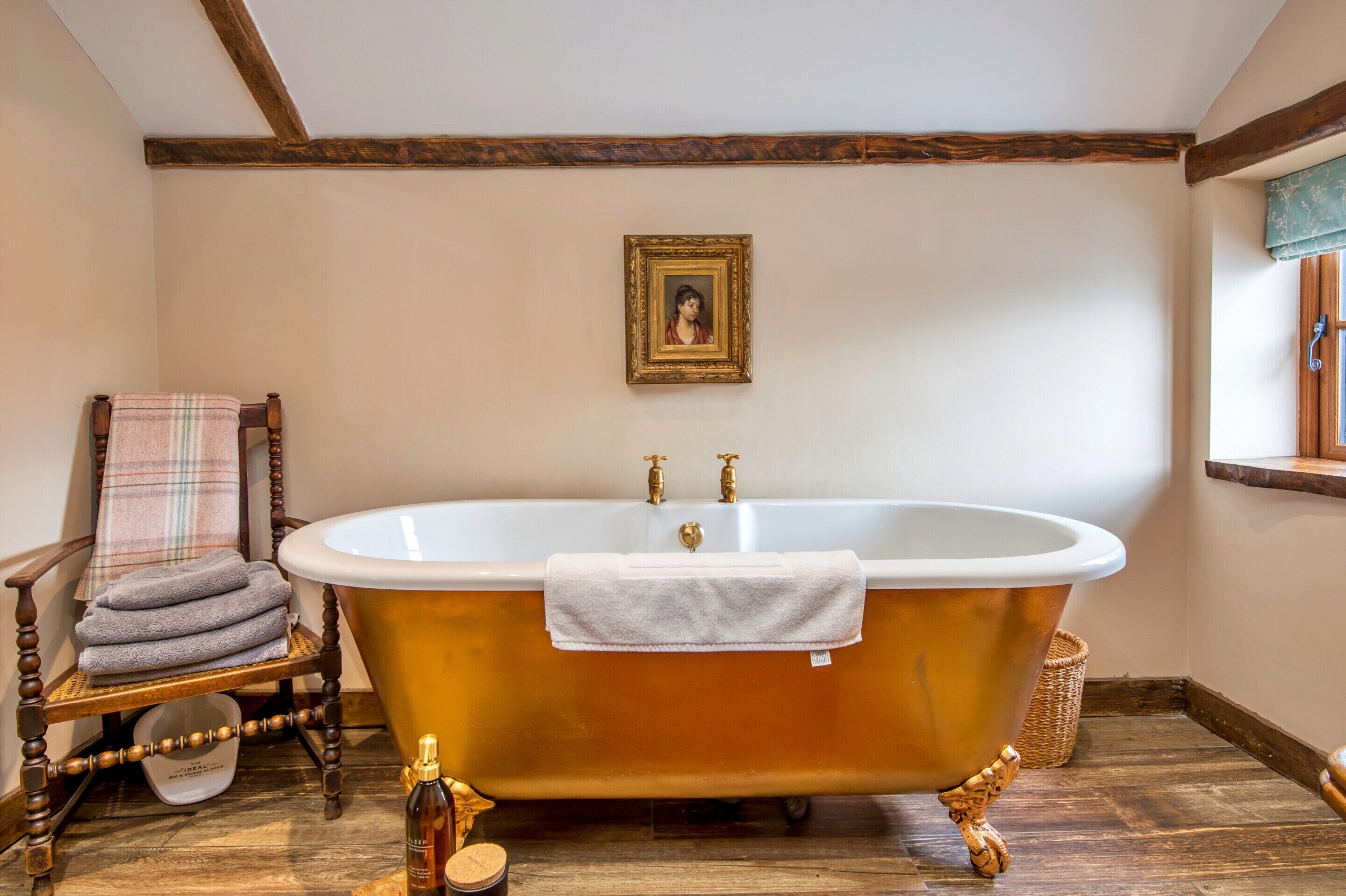 A bathroom with a freestanding bathtub, a wooden chair with a plaid towel, and a framed picture on the wall.
