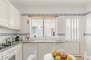 Uma cozinha com armários brancos, bancada de granito, fogão, pia e janela com vista para o exterior.