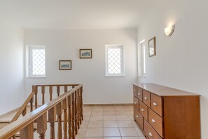 A hallway with a wooden staircase, a wooden dresser, and three windows with decorative glass panes. - #416 Spacious Villa | Private Pool, BBQ, and Parking (Albufeira)