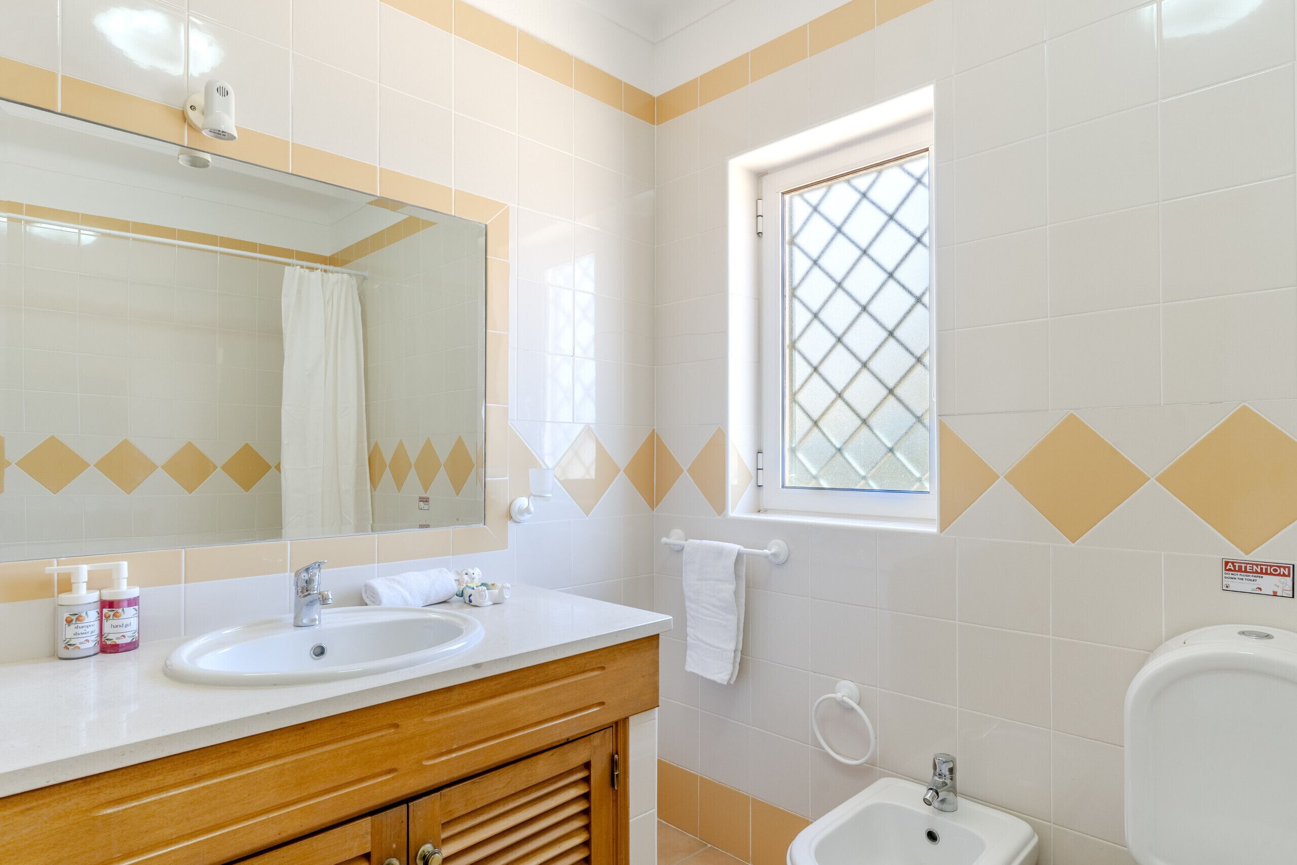 Een badkamer met een grote spiegel, twee wasbakken, een raam en een toiletbril met spuitfunctie.