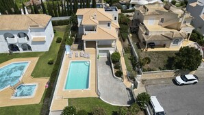 A residential area with a swimming pool, multiple houses, and a parked car. - #416 Spacious Villa | Private Pool, BBQ, and Parking (Albufeira)