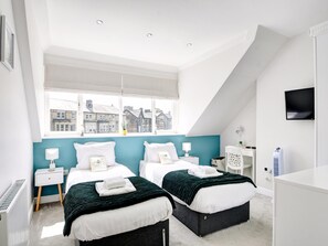 A modern bedroom with two beds, a large window with a city view, a white radiator, and a TV mounted on the wall. - Harrogate Apartment Near Bettys (Harrogate)