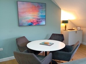 A dining area with a round table, four chairs, a painting on the wall, a lamp, and a cabinet. - Harrogate Apartment Near Bettys (Harrogate)