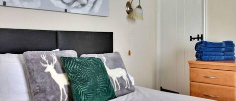 A neatly made bed with a headboard, a wall-mounted lamp, and a door with a towel rack.