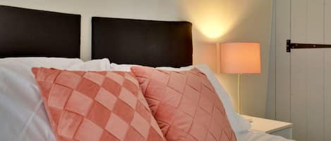 Una cama con ropa de cama blanca y dos almohadas, una con estampado a cuadros.
