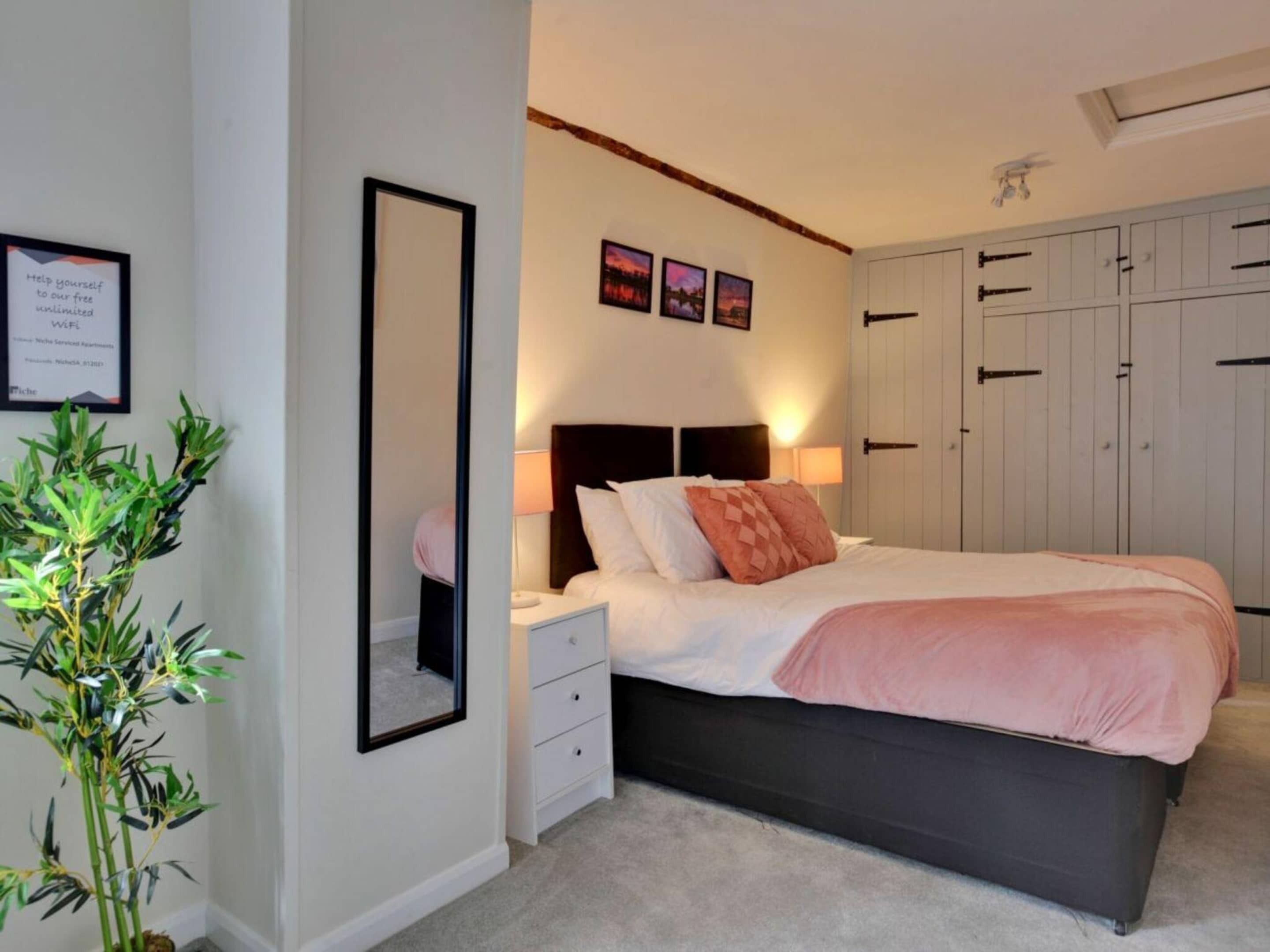 Une chambre à coucher avec un lit, des tables de chevet, un miroir, une armoire et une plante en pot.