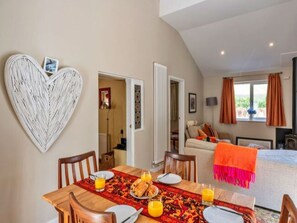 Ein Essbereich mit Wanddeko in Herzform, einem Tisch gedeckt mit Tellern, Gläsern und Orangensaft, und Blick in ein Schlafzimmer mit Bett und Vorhängen.