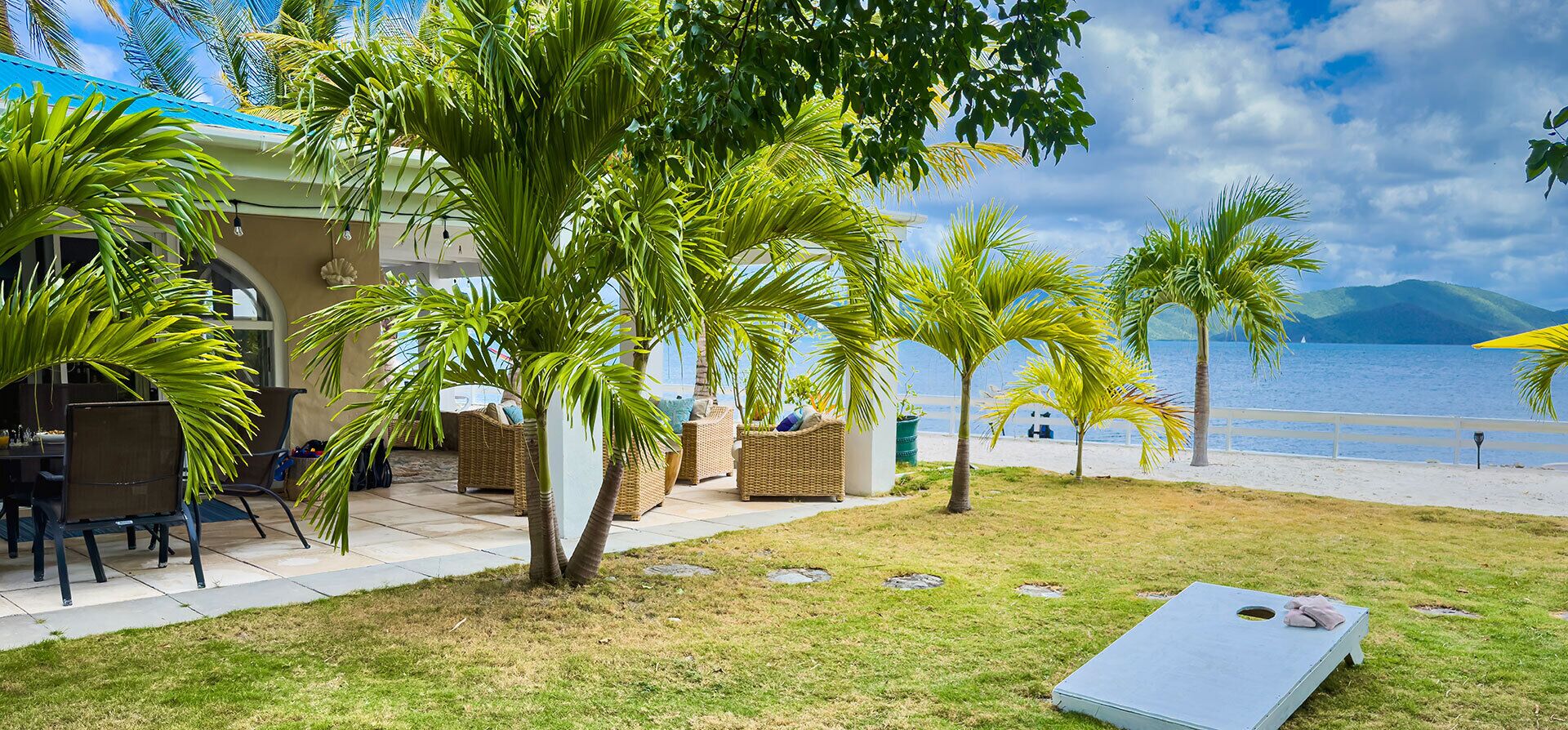 A beachfront property with outdoor seating, palm trees, and a view of the sea.