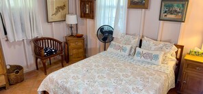 A bedroom with a bed, a chair, a nightstand, a fan, and a wall with framed pictures. - Beautiful Private Waterfront Estate, 2 Properties, 4 Bedrooms, West End Tortola (Tortola)