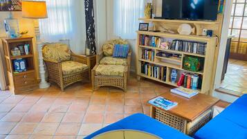 A living room with a sofa, two armchairs, a coffee table, a bookshelf, and a television.