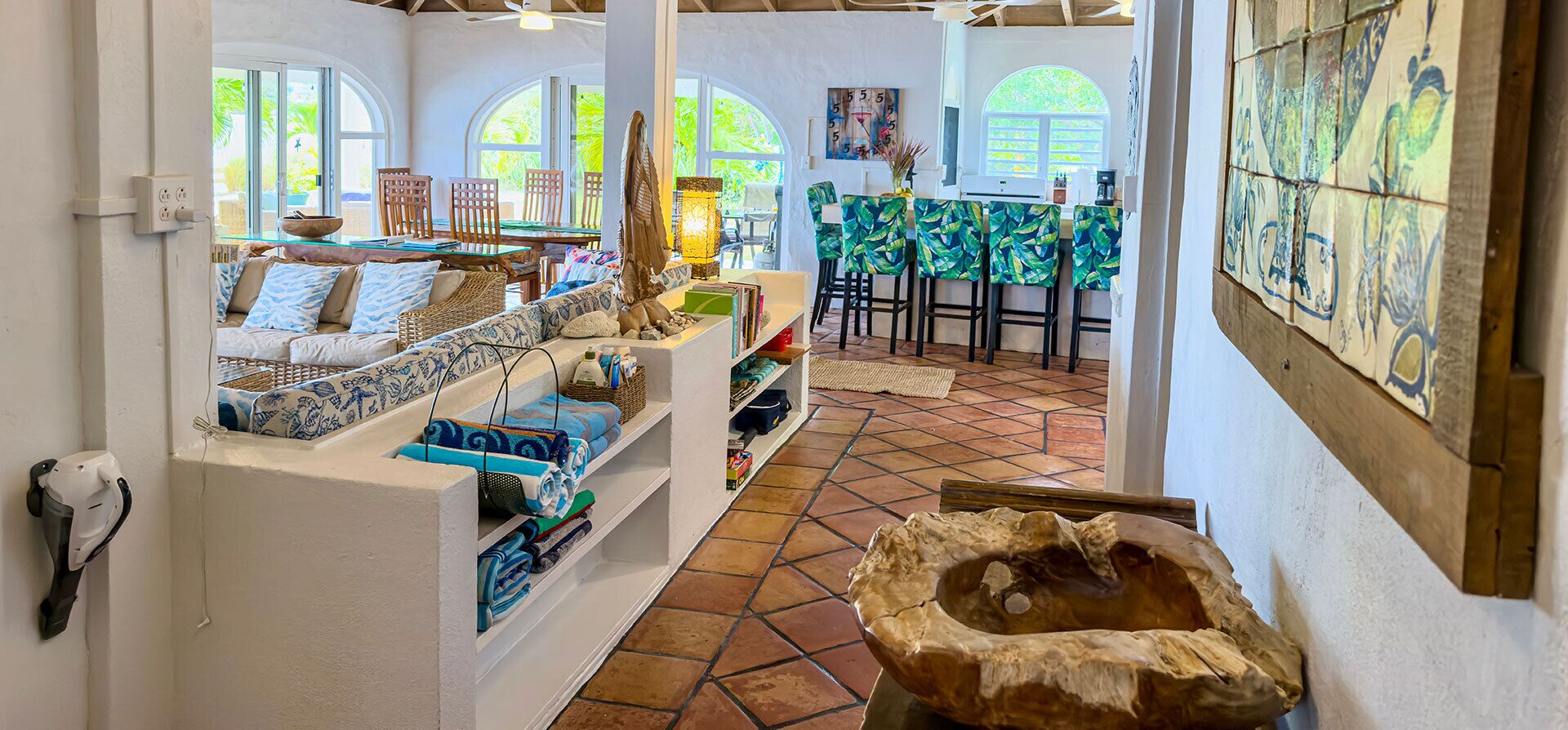 A room with a tiled floor, a wooden bowl, a sofa with patterned cushions, and a dining area with chairs and a table.