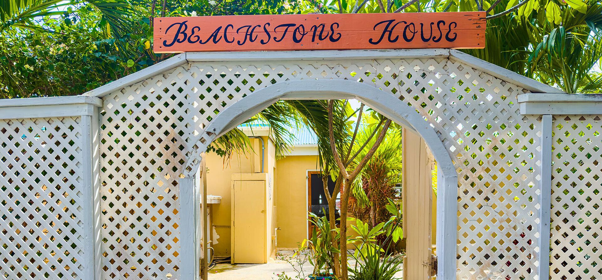 A wooden gate with a sign reading 'Beachstone House' leading to a yellow building.