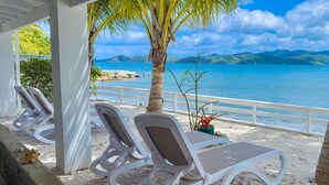 A beachside seating area with white lounge chairs and a white railing overlooking a calm sea with distant mountains. - Beautiful Private Waterfront Estate, 2 Properties, 4 Bedrooms, West End Tortola (Tortola)