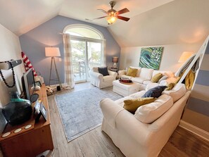 A cozy living room with a white sofa, a coffee table, and a ceiling fan. - Serenity Now: Relax by the pool! Located in the Heart of the Village. (Ocracoke)
