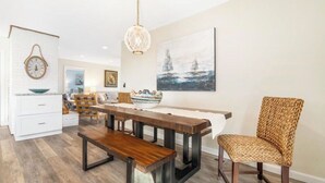 A dining area with a wooden table, benches, and a woven chair. - Charming Seaside Retreat – Walk to the Beach in Rye, NH (Rye)