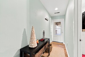A hallway with a console table, a decorative column, a small lantern, and a door leading to another room. - Atlantic Queen - Oceanfront Escape (Emerald Isle)